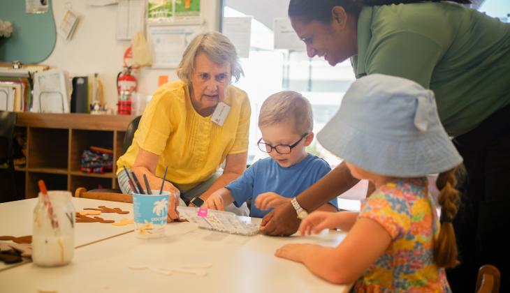 An image of two children doing craft with an older woman and an educator.